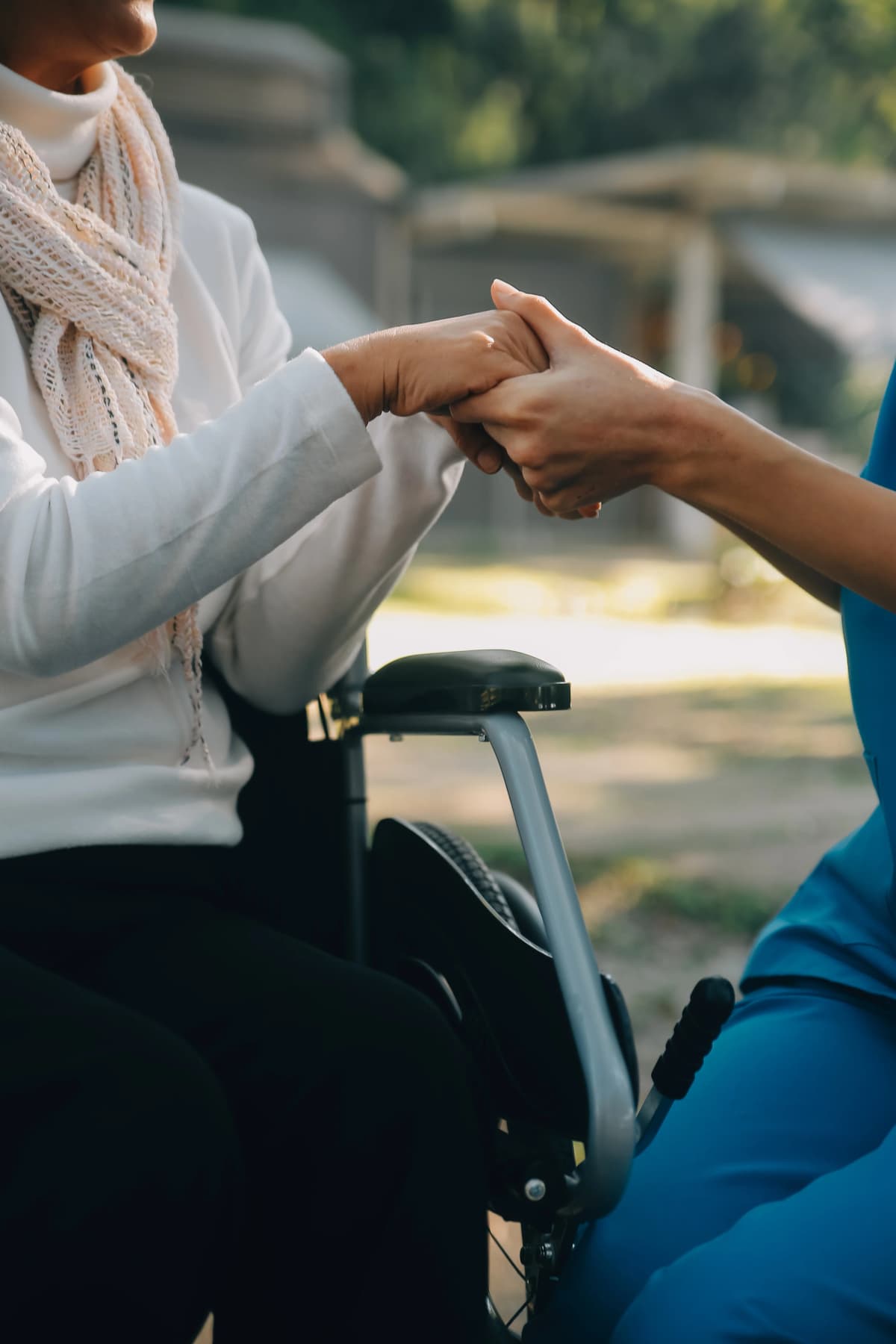 NDIS support provider assisting elderly client with wheelchair mobility equipment in garden setting - Angels Link disability support services